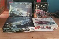 Four Monogram model kit boxes displayed on table including Metal Master Cadillac V16 sealed box, Metal Master Duesenberg SJ and Diecast Metal Duesenberg kits visible with Boattail Speedster.