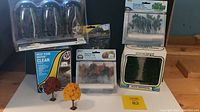 Wide shot of all miniature woodland scene items showing boxed water and multiple packs of model trees, plus loose model trees with varied foliage colors including fall colors.