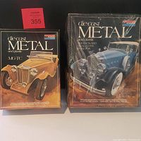 Two Monogram die-cast model kit boxes side by side: sealed 1931 Packard Dual Cowl Phaeton in plastic wrap and an MG-TC kit with opened box and visible artwork.