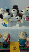 Front view of six Snoopy and Peanuts ceramic figurines and one bobblehead arranged on white cloth.