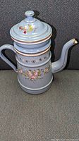 Front view of antique baby blue enamel coffee pot with floral decorations and gold trim, shows pot with lid on