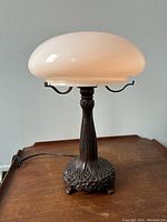 Full view of lamp showing bronzed metal tree trunk style base and white mushroom shaped glass shade on wood surface.