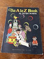 Front cover of the A to Z book showing colorful figures including a clown, mouse, and circus-themed characters on a black background.