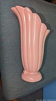 Side angle of pink pottery vase showing fluted vertical ribs, curved scalloped rim, and small circular base.