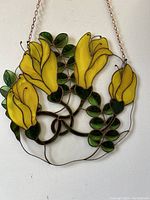 Frontal image of round stained glass panel with yellow lilies and green leaves, showing hanging chain and wire borders.