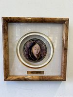 Front view of the framed medallion with wooden frame and fabric mat showing the enameled portrait inside and brass plaque with artist name.