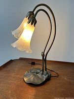 Front view of the lamp illuminated on a wooden surface showing two frosted lily-shaped glass shades and lily pad base