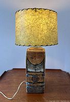 Full front view showing the lamp illuminated on a wooden surface, highlighting the glowing fibrous shade and textured pottery base.