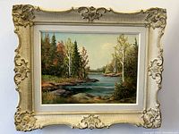 Front-facing photo showing entire framed oil painting on board depicting river landscape with forest trees in autumn colors, signed by artist.
