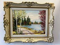 Frontal view of the fall landscape oil painting in ornate carved wood frame showing vibrant fall colors and corner wear on the frame.