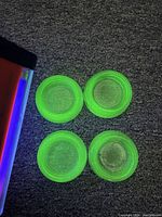 Top-down view of four round Vaseline Depression glass votive candle holders showing vibrant green color with UV light on carpet.