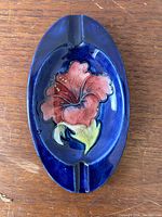 Top view of Moorcroft oval ashtray showing detailed hibiscus flower and glossy blue background