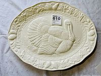 Top view of oval ceramic serving platter with raised turkey design and floral border on a fabric surface.