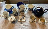 Top view of the tea set items spread on a table with mugs, teapot, creamer, sugar bowl, saucers, and a trivet.