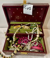 Overall view of red jewelry box open showing various necklaces, bangles and small decorative items inside.