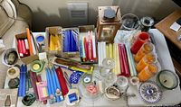 Overview photo showing all candles of various colors, pillar candles in glass, candle holders of glass and ceramic, wooden lantern, and decorative items arranged on a table.
