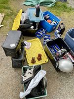 Wide view of the lot with multiple plastic containers, helmets, motorcycle saddlebags, bottle jacks, and fluids spread on the ground.