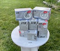 Photo showing eight boxed JIB PAR20 ceiling lights stacked on a round white table outdoors on grass.