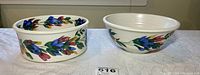 Front view of two white ceramic serving bowls with floral designs side by side on a textured white cloth surface.