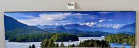 Full view of framed panoramic print mounted on a wall showing a lake with forested islands and distant snow-covered mountains.