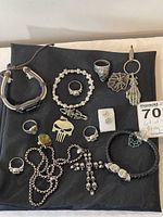 Top-down view of all skull jewelry items arranged on a black surface showing rings, bracelets, necklace, and keychain.