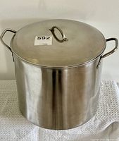 Stock pot with lid shown from the front with lid on, silver stainless steel finish, two side handles and one lid handle.