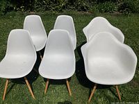 Six white molded plastic midcentury style chairs arranged outdoors on grass