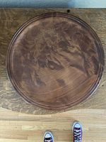 Top view of circular wooden tray displaying intricate burl wood grain pattern and polished finish, resting on wooden surface.