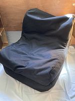 Photo showing a well-used black bean bag chair with a structured back and cushioned seat against a wooden backdrop.