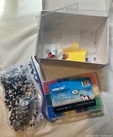 Photo of a white box containing clear plastic pegboards and a plastic container with colorful fuse beads next to a sealed bag of black and white fuse beads.