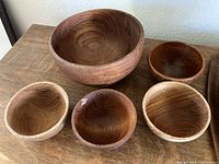 Overview photo showing one large wooden bowl and four smaller wooden bowls with natural wood grain.