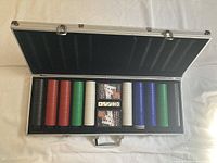 Opened aluminum poker case showing stacks of poker chips in multiple colors with decks of cards and dice.