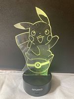 Clear acrylic Pikachu figure lit in yellow on black circular GITURKD base.