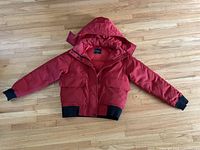Full front view of the red Everlane puffer coat laid flat on wooden floor, showing all details including hood, pockets, zipper and ribbed cuffs and waistband.