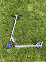 Photo of the full scooter laying flat on grass, showing blue handlebars, silver frame, and blue wheels.