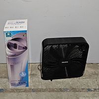 Photo showing Ionic Breeze air purifier in box next to black Pelonis fan on floor