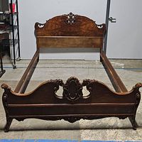 Front view of assembled wooden bed frame showing headboard, footboard and side rails on concrete floor