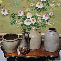 Full grouping of the four ceramic vessels on a wooden table in front of floral artwork.