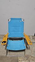 Front view of blue aluminum folding beach chair with wooden arms. Shows padded blue fabric seat and backrest, cup holder on right armrest.