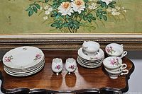 Set of six oval dessert plates stacked, six cups and saucers stacked, two small egg-shaped vases with cracks visible