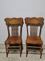Front view of both oak spindle back dining chairs showing carved top rail, spindle backs, contoured seats, turned legs and stretchers.