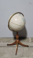 Full view of the globe on wooden tripod stand showing overall size and condition with some scuffs visible on the surface and base.