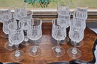Full set of 12 clear crystal wine goblets arranged on wood surface showing cut crystal design and stems.
