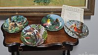 Four Knowles bird decorative plates displayed on a wooden table along with a Certificate of Authenticity.
