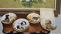 Four Knowles collector plates arranged on wooden table with certificate of authenticity included, depicting different dog breeds.