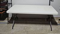Front view of the fully opened folding table showing white rectangular tabletop and black metal legs.