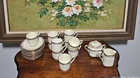 View of 10 cups with matching saucers, cream pitcher, and sugar dish arranged on wooden table