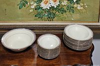 Overall view of the stacked serving bowl, fruit bowls and soup bowls on a wooden surface with floral painting background.