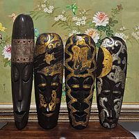Four wooden tribal masks displayed upright, showing distinct painted and carved designs and shapes