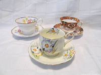 Photo displaying three Royal Albert teacup and saucer sets with distinct floral patterns and gold trim.